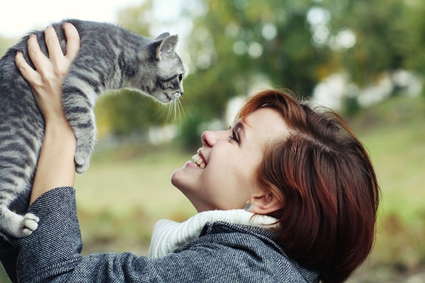 A happy woman holding a cat in the air.