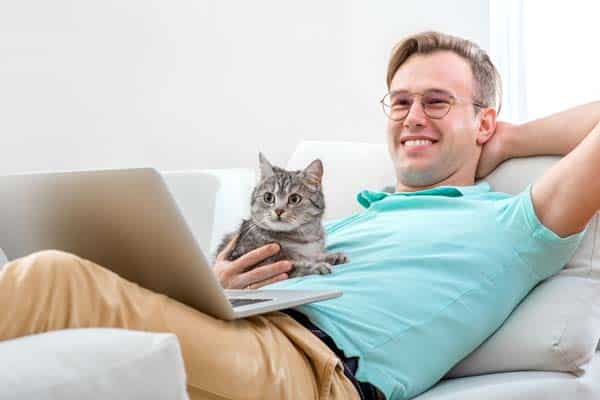 A man hangs out with a gray cat while on a laptop.