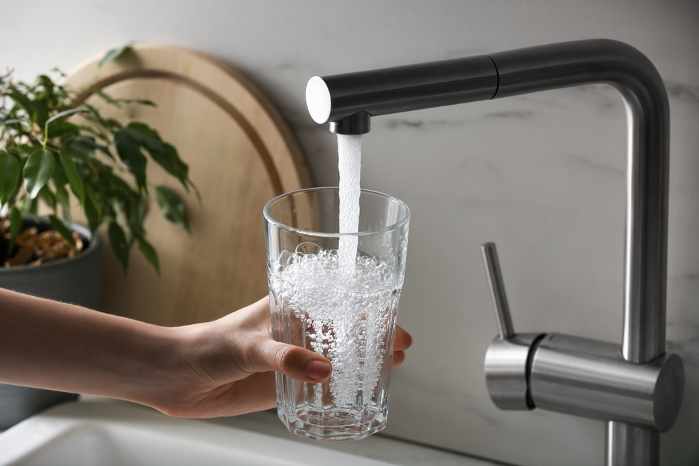 Woman filling glass with tap water from faucet in kitchen