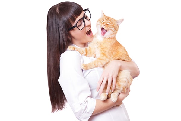 A woman in glasses singing to her ginger cat.