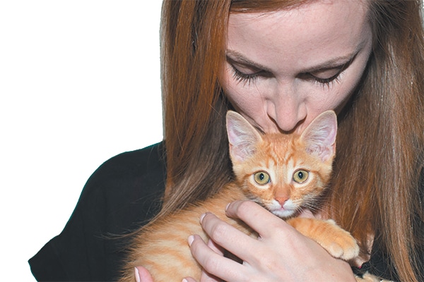 A woman kissing an orange cat.