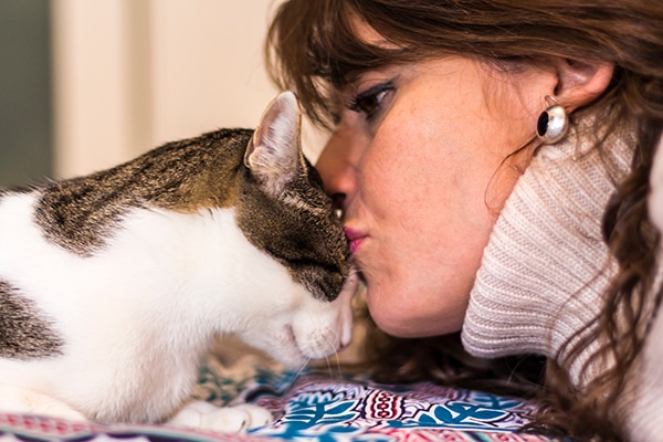 A woman in a turtleneck kissing a cat on his head.