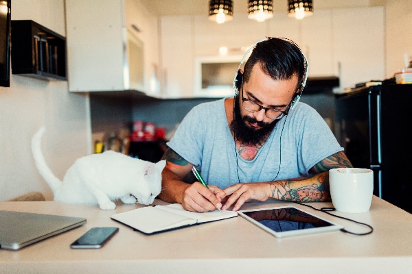 Man working on a desk with a naughty cat about to knock things over.