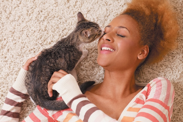 A woman kissing a cat or kitten on the floor.