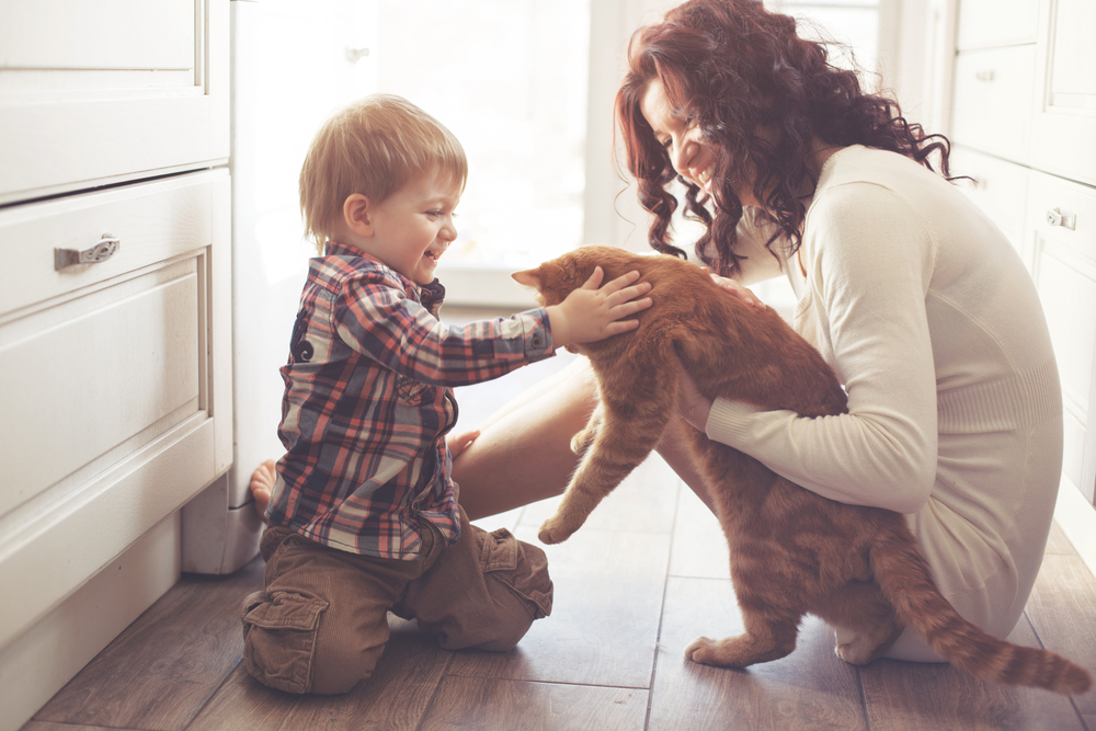 Mother with her baby playing with pet on the floor at the kitchen at home