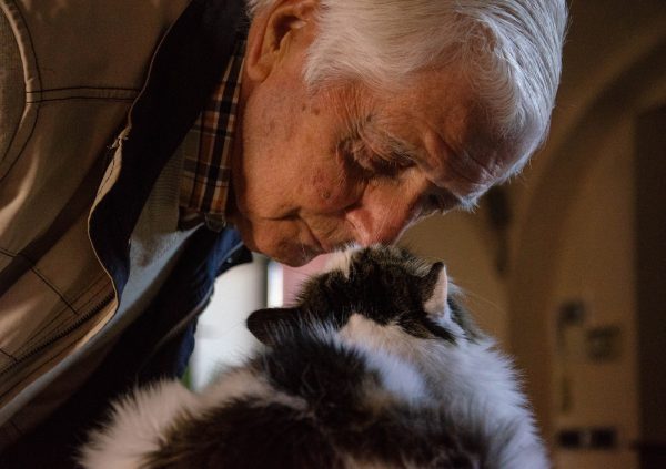 senior man in black and white jacket holding white and black cat