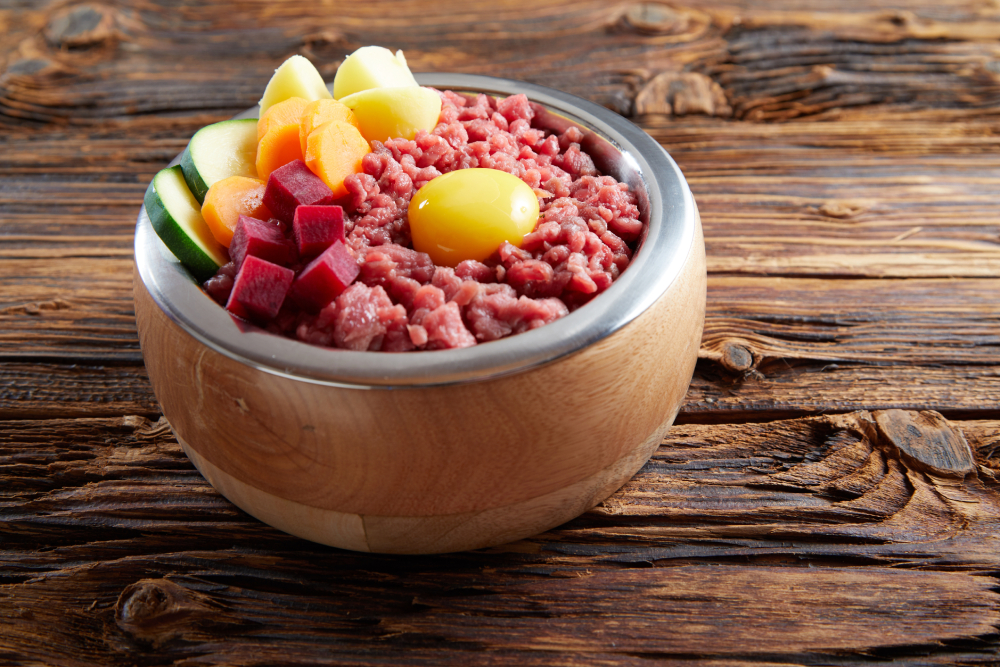 Raw food ingredients minced meat, egg and vegetables in bawl on wooden table