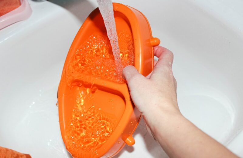 Washing animal food bowls under the tap in the kitchen sink.