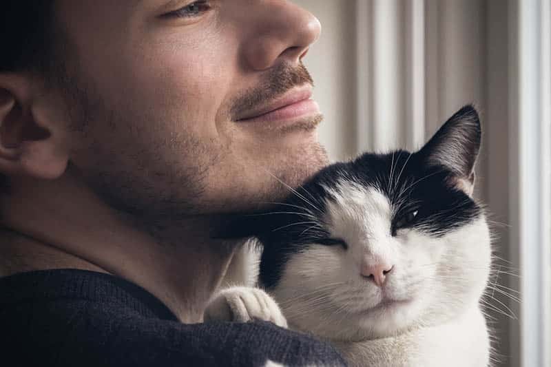 black and white cat nuzzling on man's chin