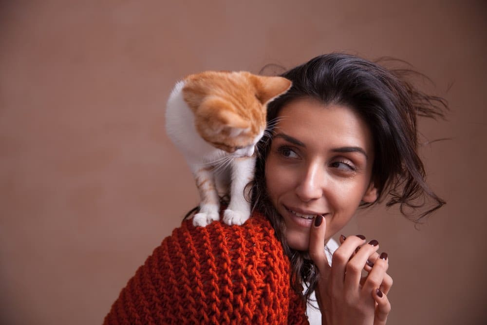 cat on woman's shoulder by head bite hair