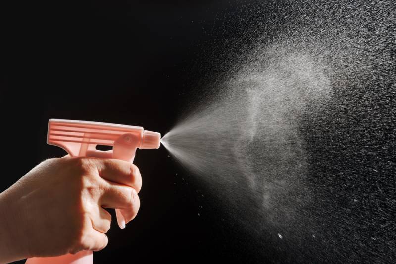 hand spraying water from a bottle on black background