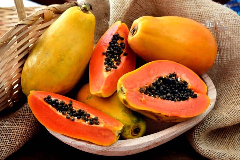 papaya fruits in a wooden pot and a straw basket and rustic fabric at the background