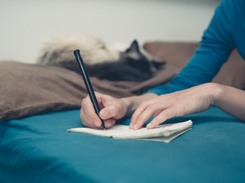 woman lying on bed with a cat writing on a notebook