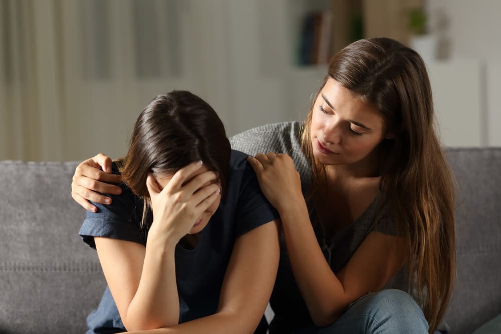 woman trying comforting another sad woman on a couch