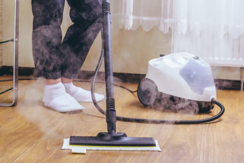 woman washes the floor in the room with a white steam cleaner