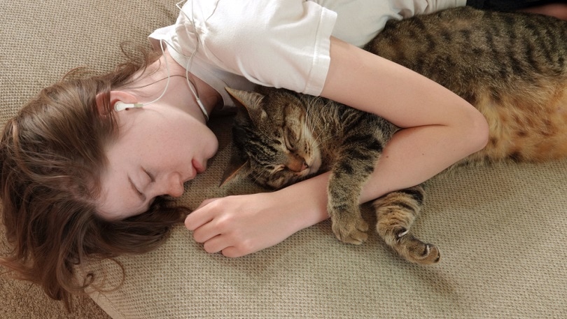 A young teen girl naps on the couch, hugging her cat