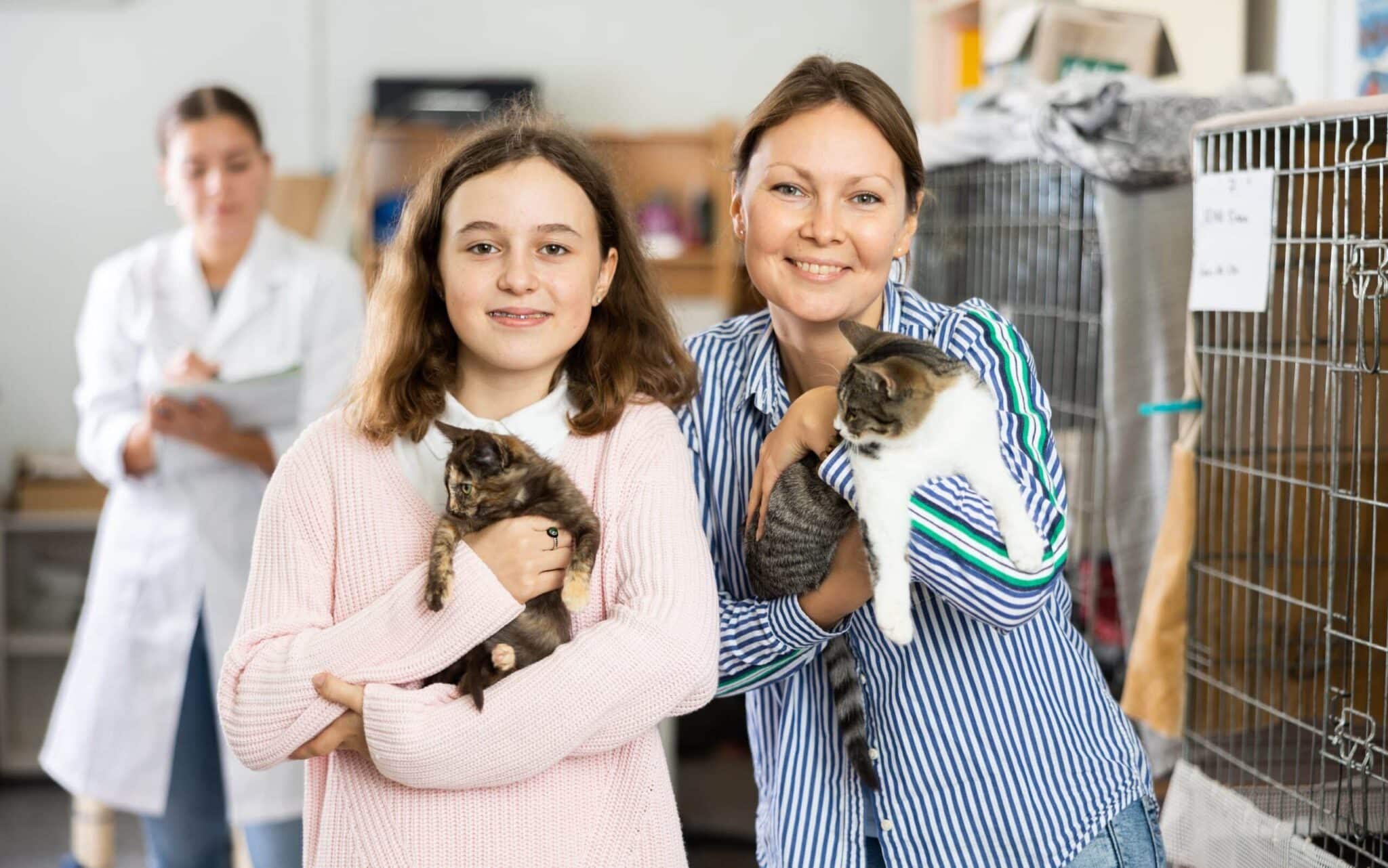 Girl and woman owners holding cats in shelter to adopt