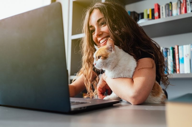 a happy woman using laptop with her cat