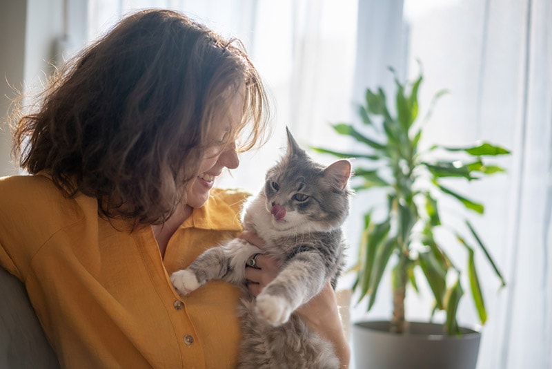 a woman holding a cat that's licking its mouth