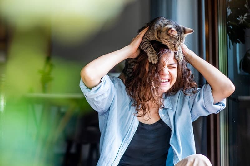 a woman laughing happily with a cat on her head