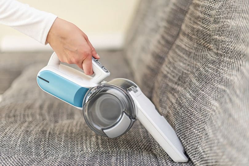 a-woman-vacuuming-furniture-in-a-house-with-a-hand-held-portable-vacuum-cleaner