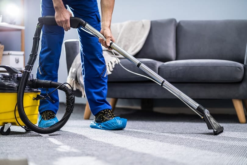 man in blue uniform cleaning carpet with vacuum cleaner