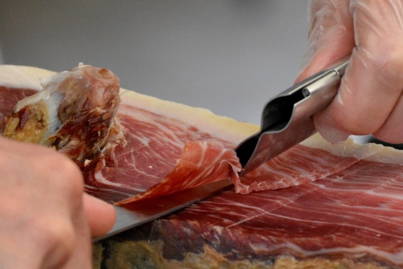 man slicing raw ham