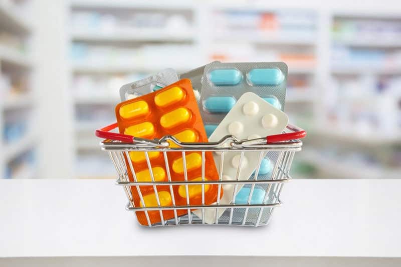 medicine pills package in shopping basket with pharmacy blurred background