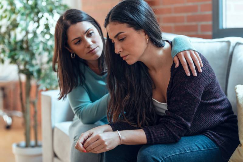 woman-comforting-her-sad-friend-while-sitting-on-the-sofa-at-home