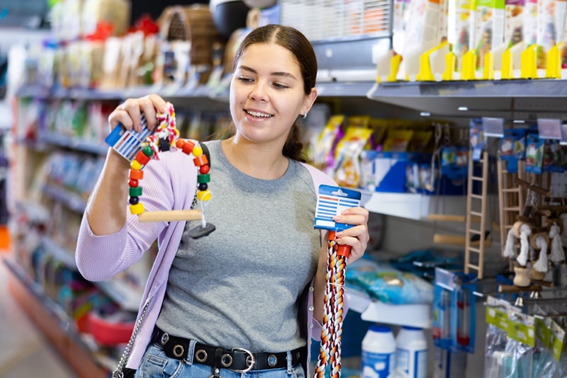 Young happy woman choosing toys for pets in pet shop