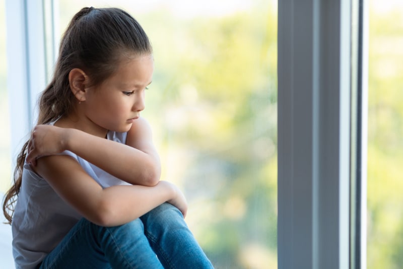 kid sitting near the window looking sad