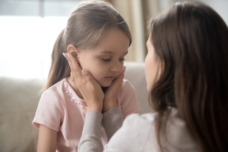 young mother touching upset little daughter face