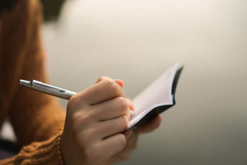 woman writing down in small white memo notebook