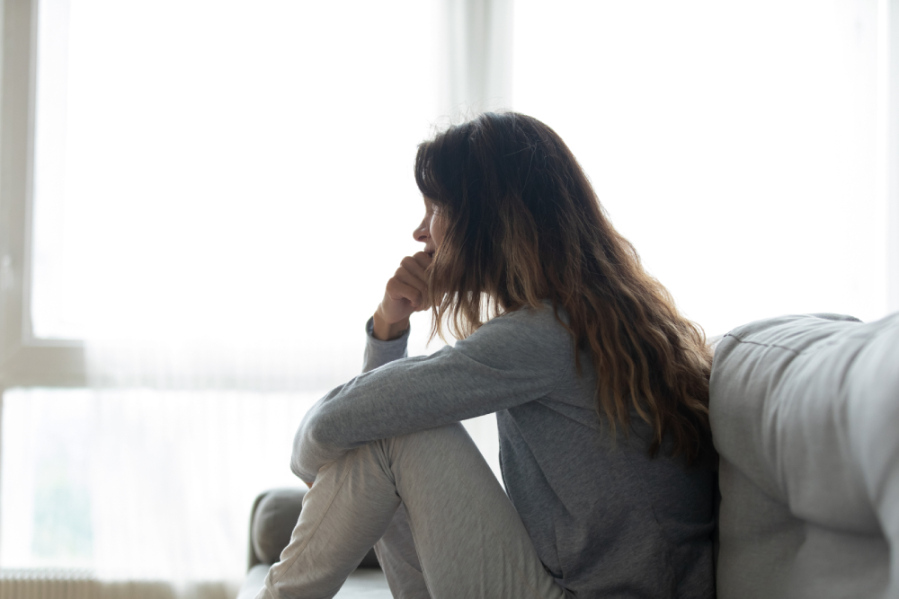 Nervous woman seated on couch lost in sad thoughts