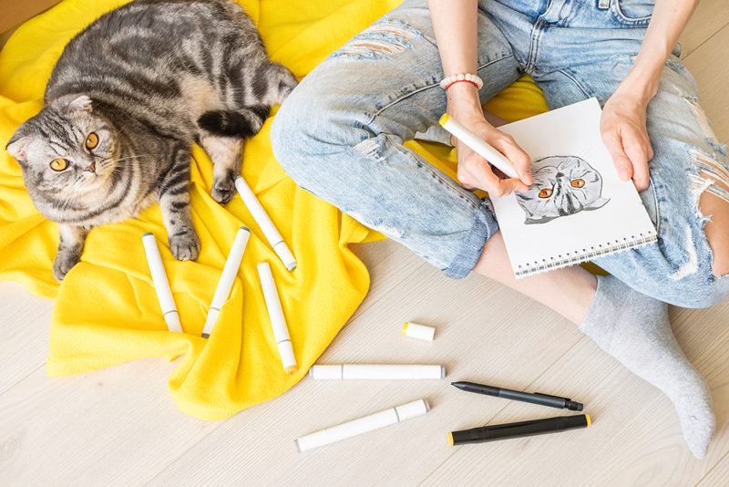 cat beside a young woman drawing a cat