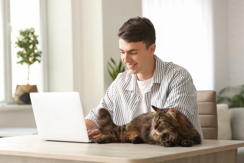 young man using laptop at table with cute cat